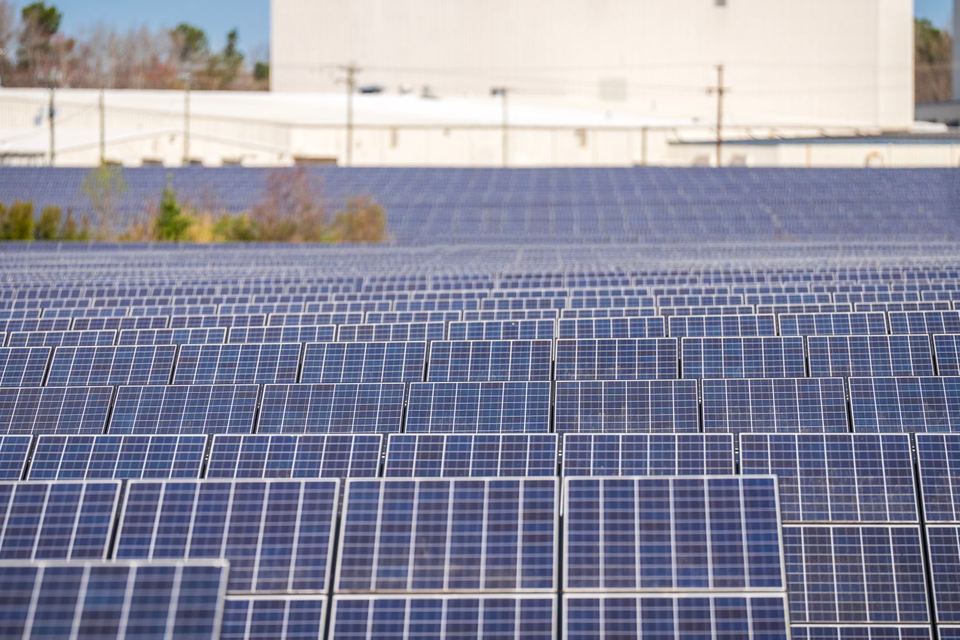 Usina fotovoltaica de solo com fileiras de módulos ao lado de estruturas — imagem ilustrativa de banco (Mark Stebnicki / Pexels), não é obra da E5